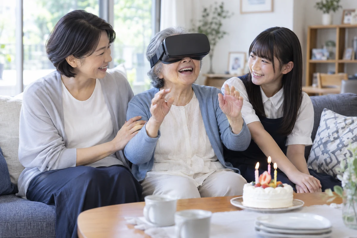 誕生日にVR旅行を楽しむ祖母と、笑顔で寄り添う娘・孫娘のイメージ